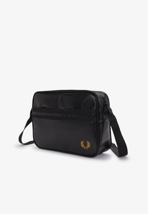 Bolso de hombro rectangular negro con logo de laurel dorado, bolsillo frontal con cremallera y correa ajustable sobre fondo blanco.