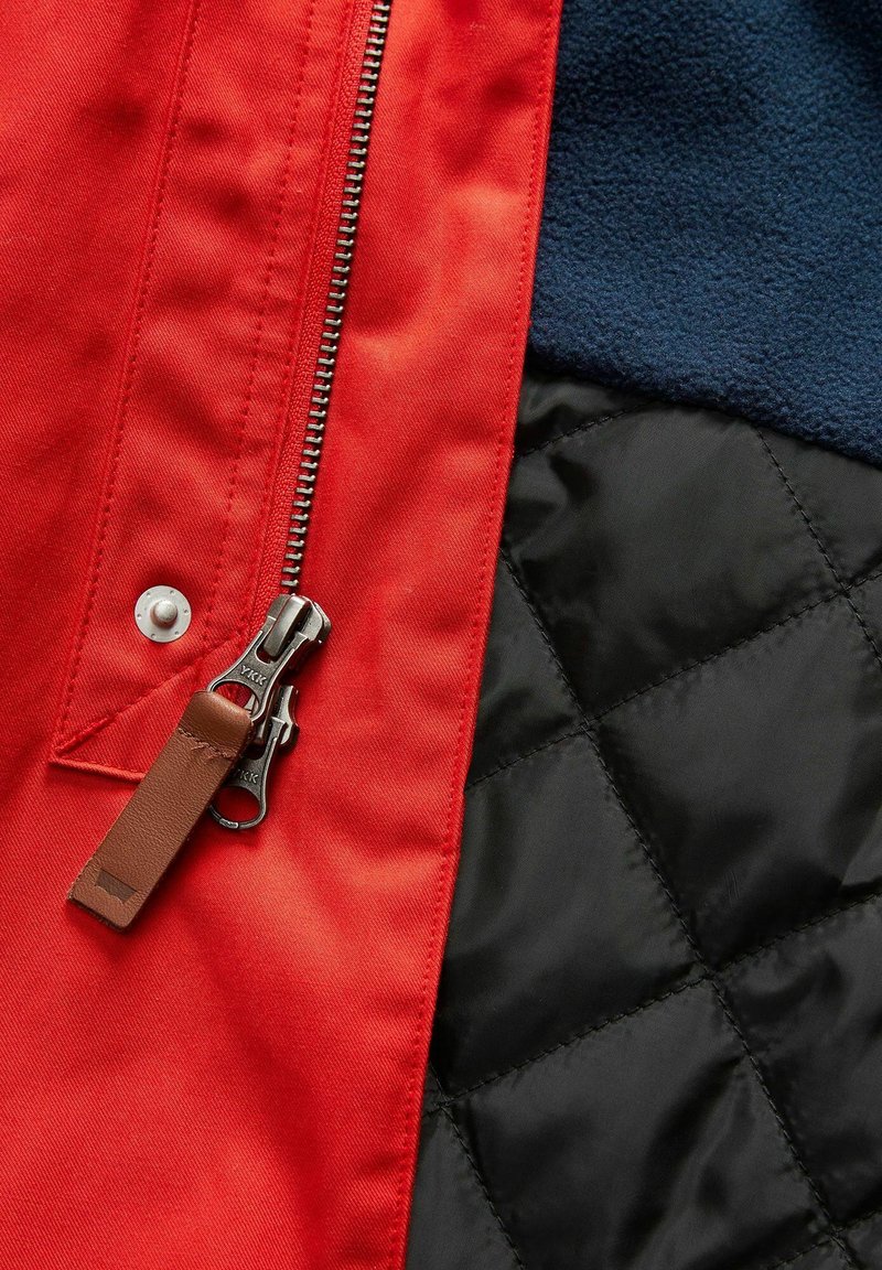 Rode jack met een zilveren rits, leren trekker en marineblauwe fleece. Zwarte gewatteerde paneel heeft een ruitpatroon.