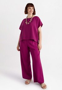 Completo magenta in due pezzi composto da una blusa larga a maniche corte e pantaloni a gamba larga, realizzato in tessuto leggero, abbinato a una collana di perle.