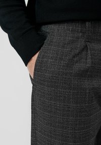 Spodnie w kratę w odcieniach szarości z subtelnym wzorem, z boczną kieszenią oraz mankietem ciemnego swetra przy materiale.