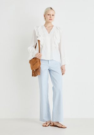 Valge pika varrukaga pluus ruffle-detailedega, koos siniste ja valgete triibuliste laiade pükstega. Õlal on pruun sametist frantsi kott.