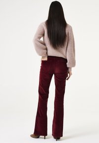 Burgunderfarbene Cord-Flared-Hosen mit Gesäßtaschen, kombiniert mit einem hellrosa gerippten Strickpullover mit langen Ärmeln und einem lockeren Schnitt.