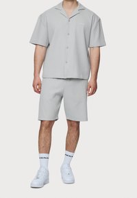 Grijze short-sleeve overhemd met knopen en bijpassende korte broek, beide van textuur met ribstof; gedragen met witte sneakers en sokken.