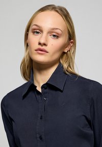 Navyblauwe button-up shirt van gladde stof met een gestructureerde kraag, voorzien van een subtiele logo-geborduurde op de borst en zwarte knopen.
