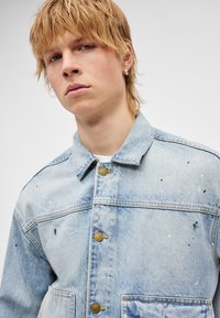 Ανοιχτό μπλε τζιν μπουφάν με γιακά, κουμπιά εμπρός και τσέπες. Διακοσμημένο με πιτσιλιές χρώματος σε διάφορες αποχρώσεις για επιπλέον λεπτομέρεια.