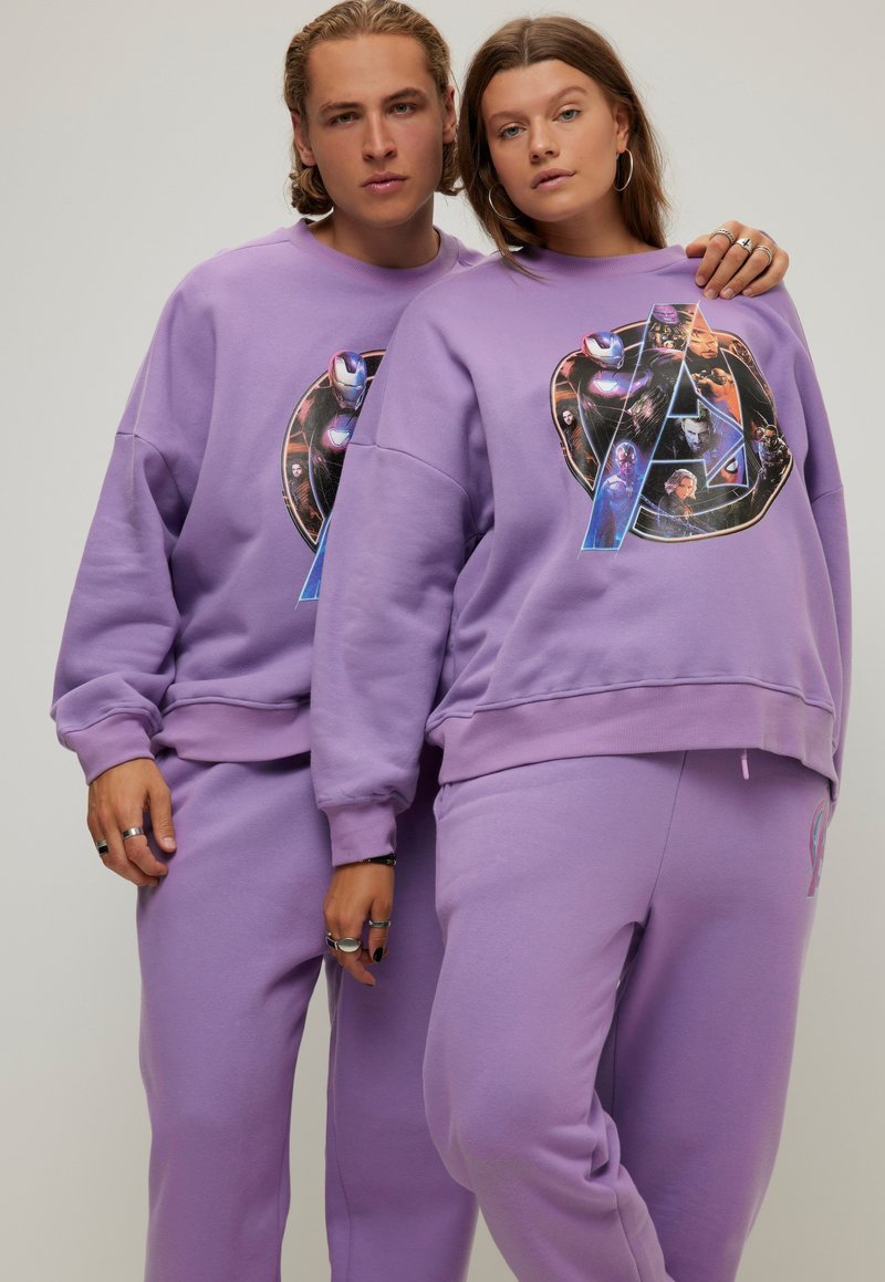 Paarse sweatshirt en sweatsuit set van zacht materiaal. Bevat een groot grafisch ontwerp met figuren, een rond logo en geribbelde manchetten.
