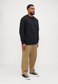 Svart sweatshirt med rund halsringning och ribbade ärmslut, tillsammans med beige byxor. Sneakers är svarta med vita sulor och snören.