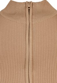 Beige ribbad tröja med hög krage och hel dragkedja bak. Har en mjuk textur och snyggt avslutade kanter.