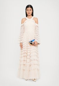 Maxi jurk in lichtroze, met gewatteerde ruffles, off-shoulder mouwen en een fitted taille. Vergezeld van een metallic clutch.