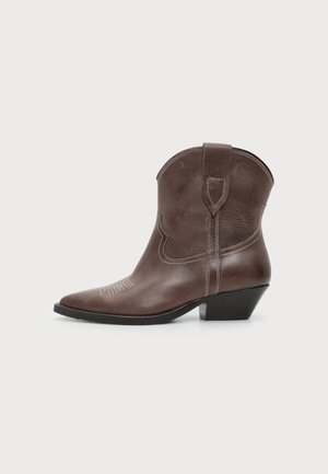 Botte cowboy marron en cuir à la cheville, avec bout pointu, couture décorative, bride latérale, et talon bas incliné sur fond blanc.