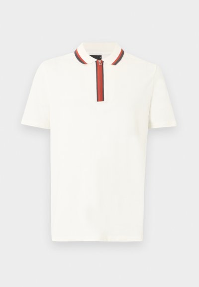 Λευκό πόλο με κοντά μανίκια και φερμουάρ στον γιακά, με κόκκινες και μαύρες ρίγες στην τρύπα του φερμουάρ και στην άκρη του γιακά.