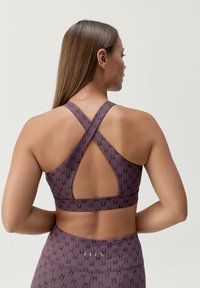Sujetador deportivo morado con diseño de espalda cruzada, patrón sutil y una tela suave y texturizada.