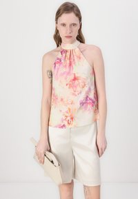 Kort halterneck topp i pastel blomstertrykk med nyanser av rosa, oransje og krem; kombinert med lyse beige shorts og en matchende clutch.