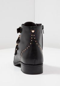 Botte de cheville en cuir noir avec des zips latéraux, des boucles en argent et des accents cloutés en or rose, présentant un petit détail en forme de cœur à l'arrière.