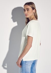Lys grøn, kortærmet bluse med afslappet pasform, sideslidser og glat tekstur, vist sammen med lyseblå denimjeans.