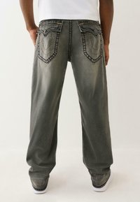 Osoba ubrana w luźne czarne, wyblakłe dżinsy z ozdobnym przeszyciem na tylnych kieszeniach, w połączeniu z białymi butami i białą koszulą.