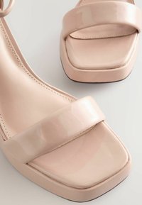 Lyserøde laklæder højhælede sandaler med firkantet tå, bred rem foran og glat finish.