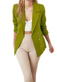 Zielona, dwurzędowa marynarka z klapami z wycięciem, usztywnionymi ramionami i srebrnymi guzikami, zestawiona z beżowymi, spodnia wysokim stanem.