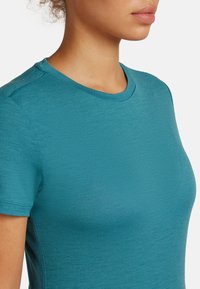 Teal T-shirt met korte mouwen en een ronde halslijn, voorzien van een soepele textuur en subtiele glans. De stof heeft een lichte, ademende kwaliteit.
