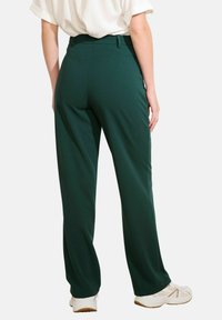 Pantaloni larghi verdi realizzati in tessuto liscio, con vita alta e dettagli discreti su tasche posteriori, abbinati a sneakers bianche.