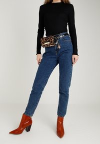 Czarna bluzka z długim rękawem, niebieskie dżinsy z wysokim stanem, nerka w panterkę oraz pomarańczowe botki z lakierowanej skóry na słupku.