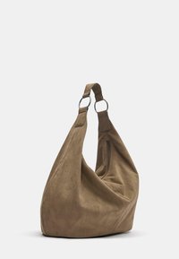 Mjuk brun mocka hobo-väska med bred axelrem fäst vid två metallringar och en sidoficka med dragkedja, som vilar på en vit yta.