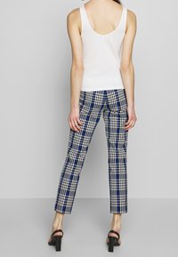 Top bianco senza maniche con schiena a scollo abbinato a pantaloni attillati a scacchi blu, neri e bianchi. Modella con sandali neri con tacco alto.