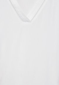 Chemise blanche à col en V, tissu lisse, bordure texturée discrète le long de l'encolure, légère avec un design épuré et simple.