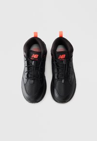 Une paire de baskets New Balance noires avec des languettes orange et des lacets à tirage rapide, vue d'en haut sur un fond clair.