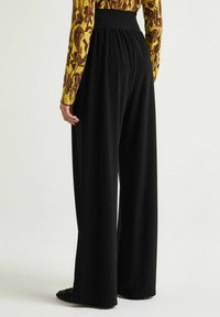 Pantaloni neri a gamba larga con vita arricciata, caratterizzati da una texture liscia e un tessuto fluente. La vista posteriore mette in evidenza la vestibilità ampia.