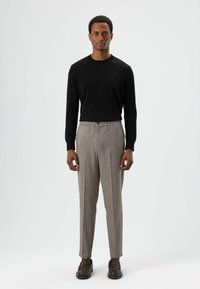 Zwarte top met lange mouwen gecombineerd met lichtgrijze broek met ruitpatroon, voorzien van een taille met aantrekkoord en een knoop, afgerond met donkere loafers.