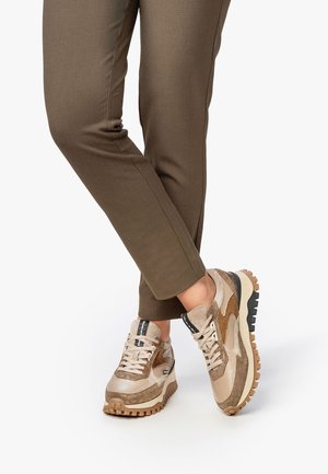 Beige sneakers met gemengde texturen, voorzien van suède en leren accenten, donkere veters en een robuuste rubberen zool met een uitgesproken loopprofiel.