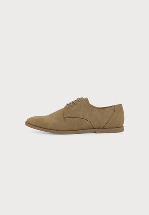 Chaussure Oxford en daim marron à lacets avec semelle plate et bout arrondi, vue de côté sur un fond clair uni.