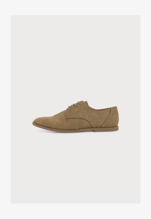 Chaussure Oxford en daim marron à lacets avec semelle plate et bout arrondi, vue de côté sur un fond clair uni.