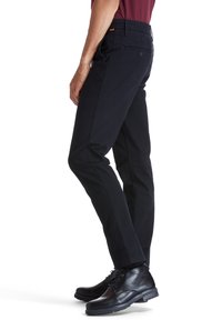 Black, slim-fit pants with a smooth texture and front pockets, paired with black leather shoes. Features a button closure and orange accents.