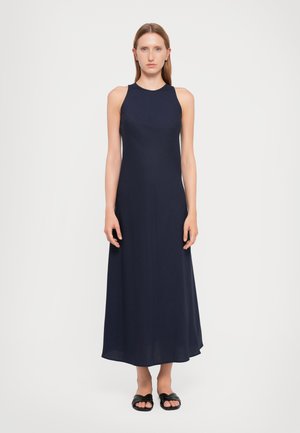 Navy maxi dress with a high neckline, fitted bodice, and flowy skirt. Made from a smooth fabric, paired with black slide sandals.