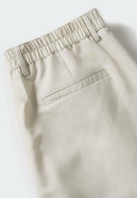 Lichtbeige broek met een elastische tailleband, voorzien van een enkele achterzak en een gladde, gestructureerde stof.