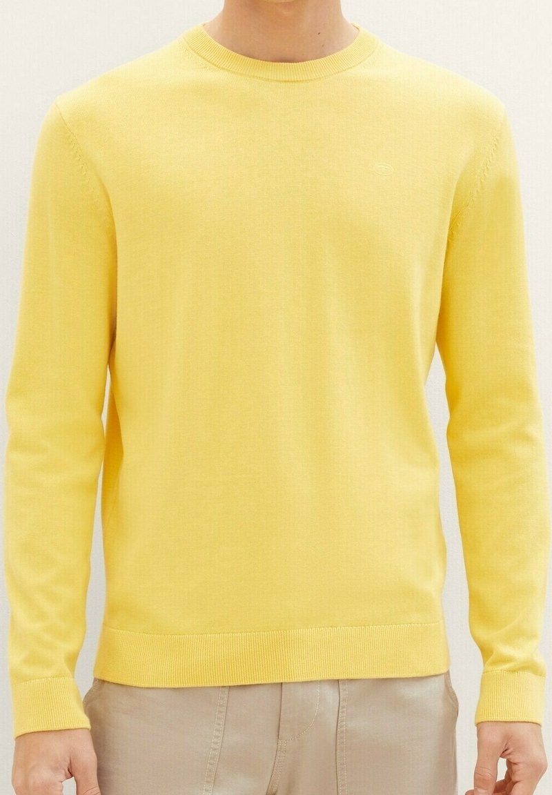 Gelber Strickpullover mit Rundhalsausschnitt, langen Ärmeln sowie gerippten Bündchen und Saum. Hergestellt aus weichem Stoff, mit einem dezenten Logodetail.