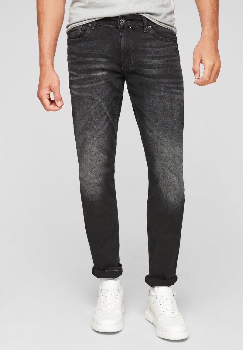 Jeans de mezclilla negra con un corte ajustado, que presentan un desgaste en los muslos, cinco bolsillos y un puño vuelto, combinados con zapatillas blancas.