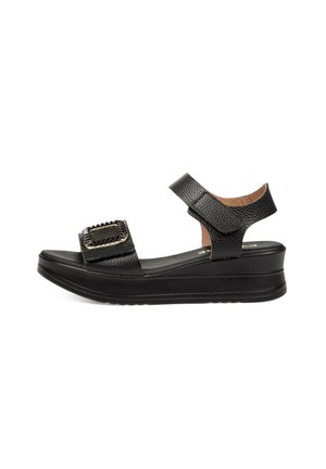 Sandalia cuña de cuero negro con tiras de velcro en el tobillo y la parte frontal, detalle texturizado en la hebilla y suela acolchada.