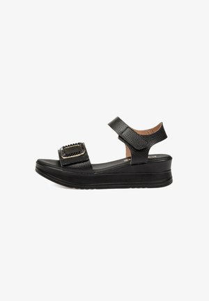 Sandalia cuña de cuero negro con tiras de velcro en el tobillo y la parte frontal, detalle texturizado en la hebilla y suela acolchada.