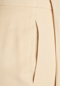 Tecido bege com uma superfície texturizada, apresentando um bolso lateral incorporado no design. Linhas limpas e detalhamento mínimo.