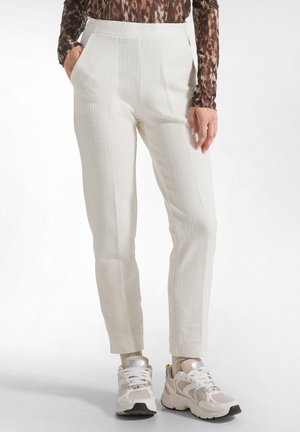 Pantalones blancos texturizados de talle alto, con bolsillos laterales y corte ajustado, combinados con zapatillas deportivas beige y blancas.