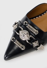 Black leather pointed-toe shoe with silver hardware accents, including spiral details and decorative buckles. Interior features striped pattern.