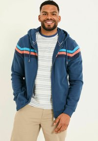 Navy hooded sweatshirt with horizontal stripes in teal, coral, and dark blue. Worn over a light striped t-shirt. Cotton blend material.