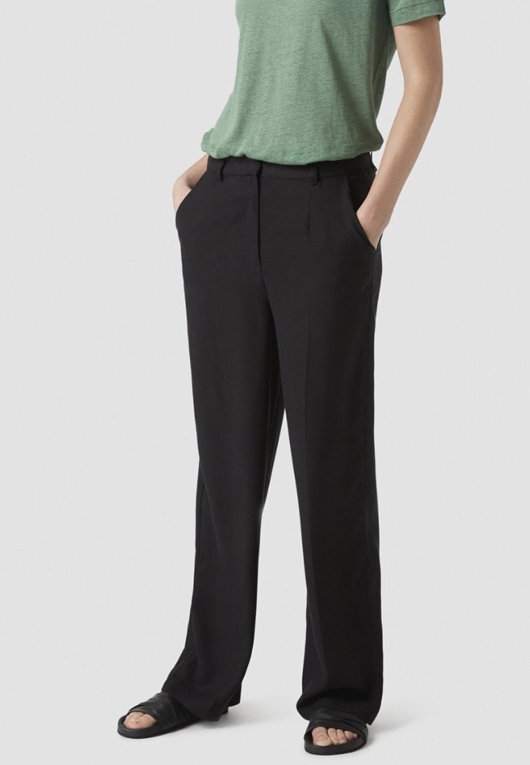 Svarta byxor med rak bendesign, har sidofickor, midje i medelhöjd och slät tygtextur. Kombineras med en grön t-shirt.