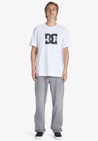 Bílý bavlněný tričko s černým logem DC. V kombinaci se světle šedými džíny a černými teniskami. Jednoduchý, ležérní design.