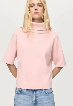 Jasnoróżowy sweter krótki z rękawami, z dekoltem typu cowl, wykonany z miękkiego, strukturalnego materiału. Fason jest luźny i nieco skrócony.
