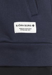 Tessuto sportivo blu navy con una superficie liscia; presenta un'etichetta bianca con il testo "BJÖRN BORG" e "PREMIUM SPORTSWEAR".