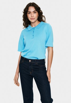 Polo shirt azzurro chiaro a maniche corte con colletto, dotato di una placca con tre bottoni. Indossato con jeans di denim blu scuro.